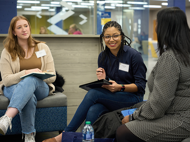 Image of two female students speaking with an admissions counselor at a graduate event.