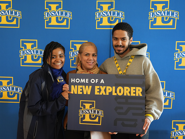 Image of three people posing with a "Home of a New Explorer" lawn sign.