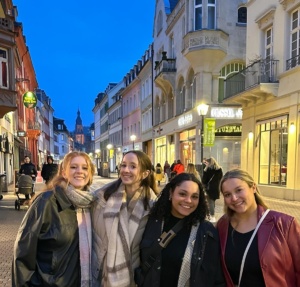 Image of four female students on a street with shops in the background.