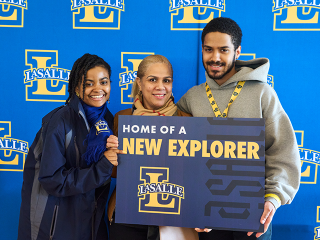 Image of a student, parent, and an admissions counselor holding a "Home of a new Explorer" sign.